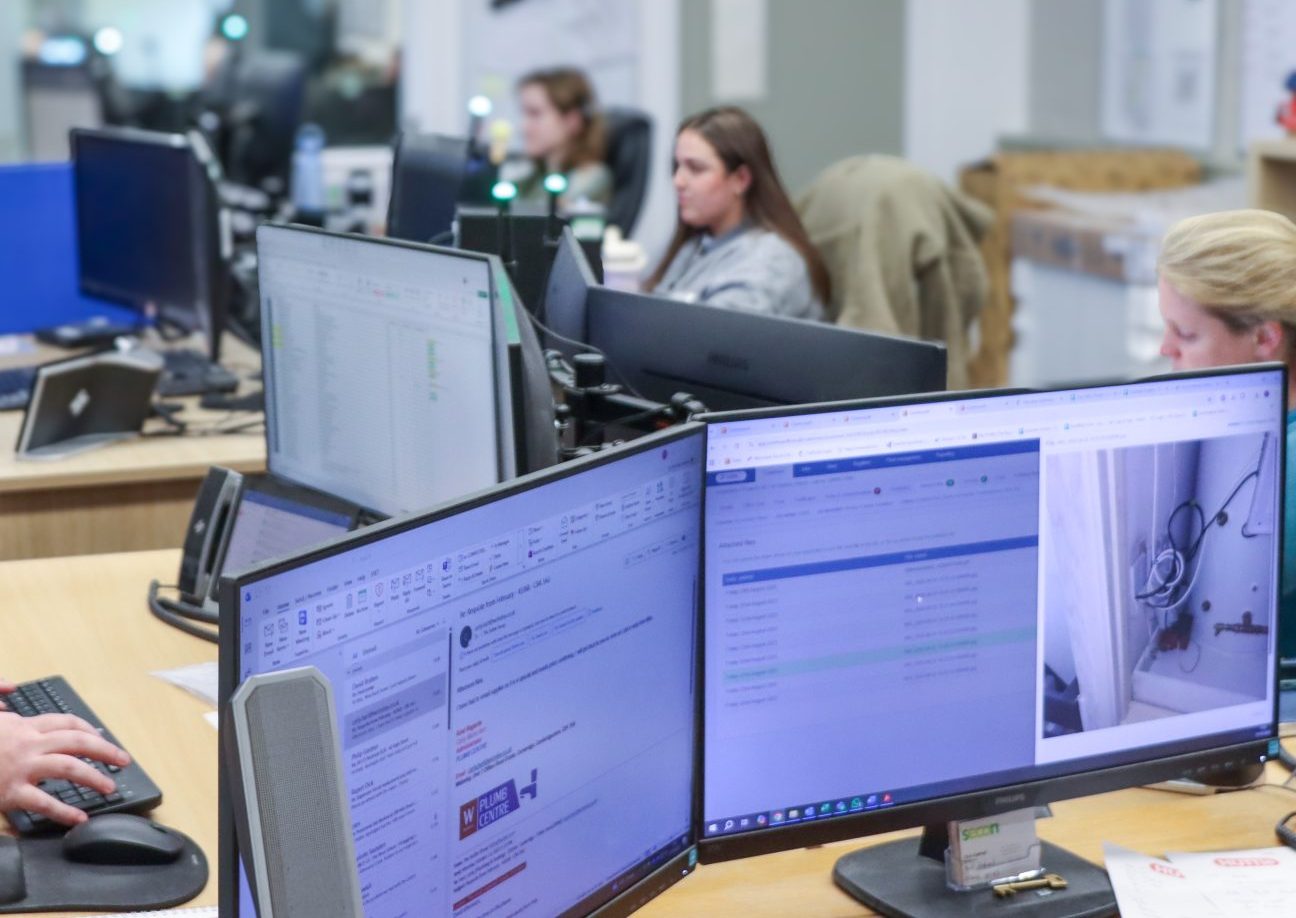 An employee's computer and office staff working in the background
