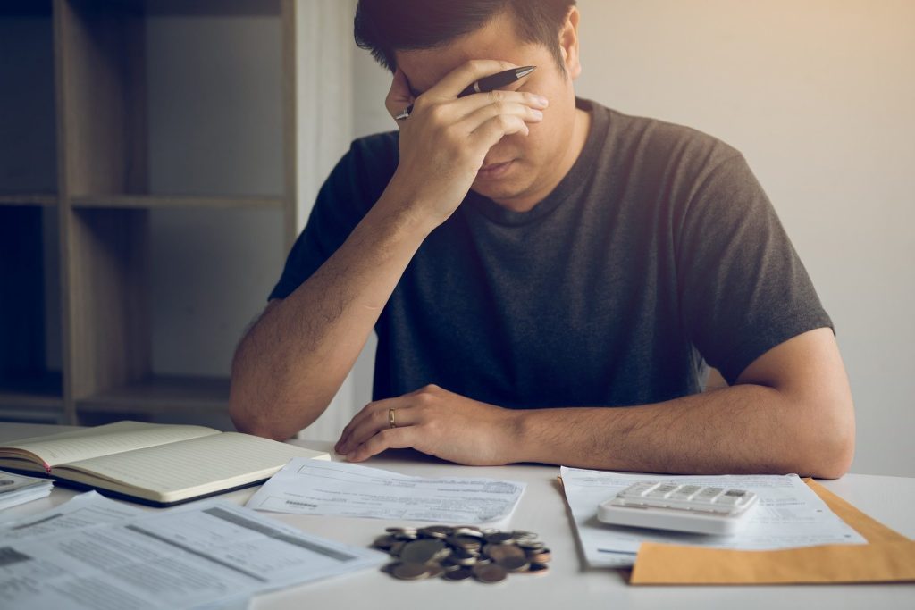 Person sat at a table stressed about money, with invoices, physical coins and a calculator in front of them