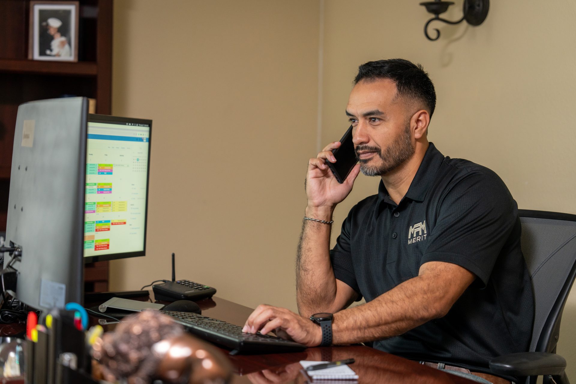 Merit Facility Management team member on their phone and using their computer at their desk