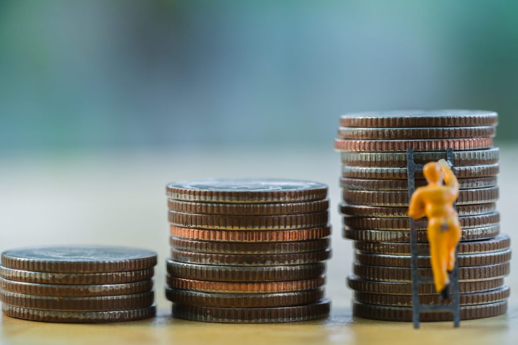 Three piles of money and a small figure climbing up a ladder on the biggest pile