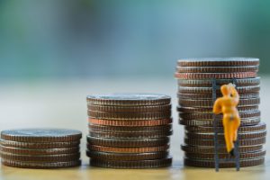 Three piles of money and a small figure climbing up a ladder on the biggest pile