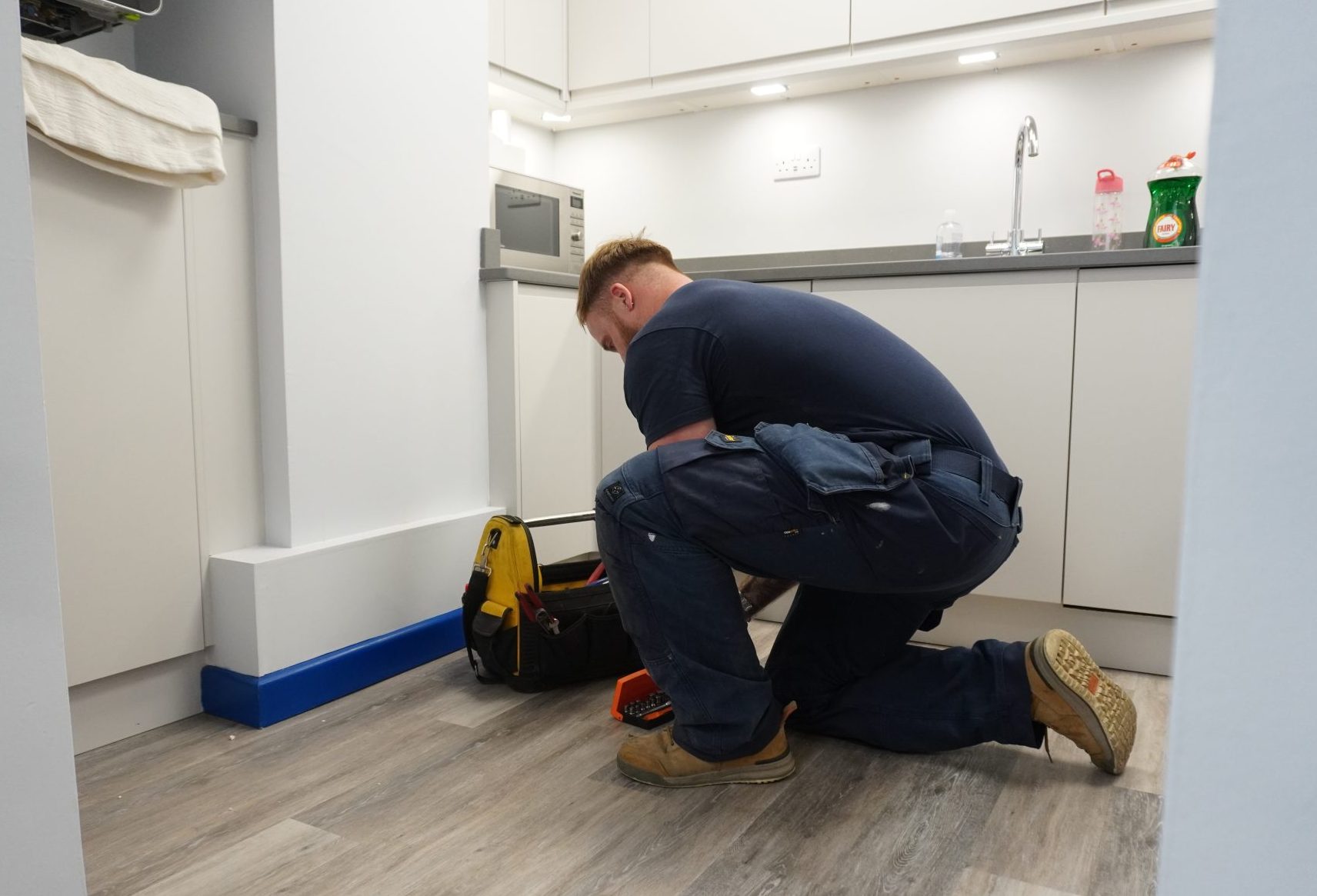 Engineer knelt down organising their toolkit in a kitchen