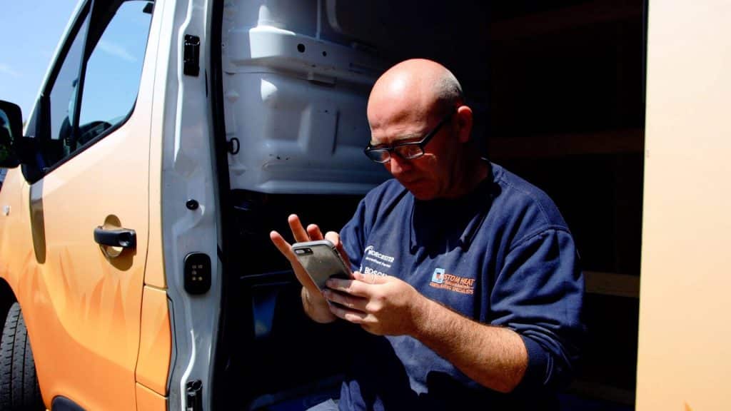Custom Heat engineer sitting in van looking at mobile phone