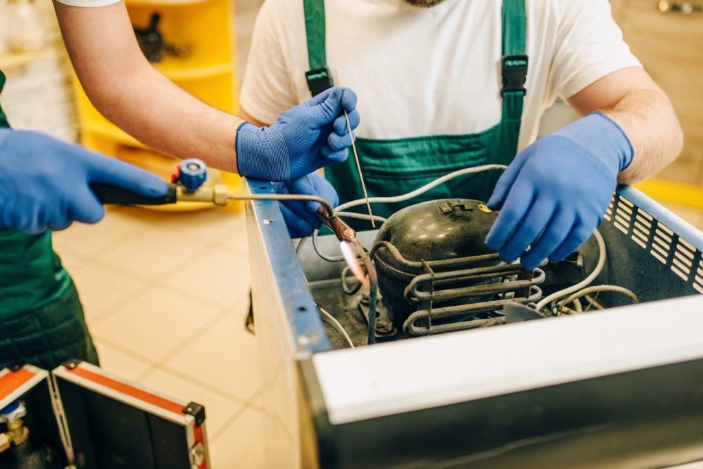 Two workers repairing a refrigerator